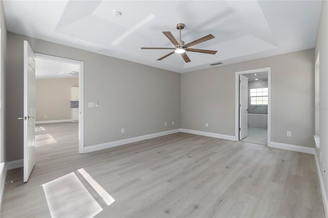 unfurnished bedroom featuring a tray ceiling, baseboards, visible vents, and light wood finished floors