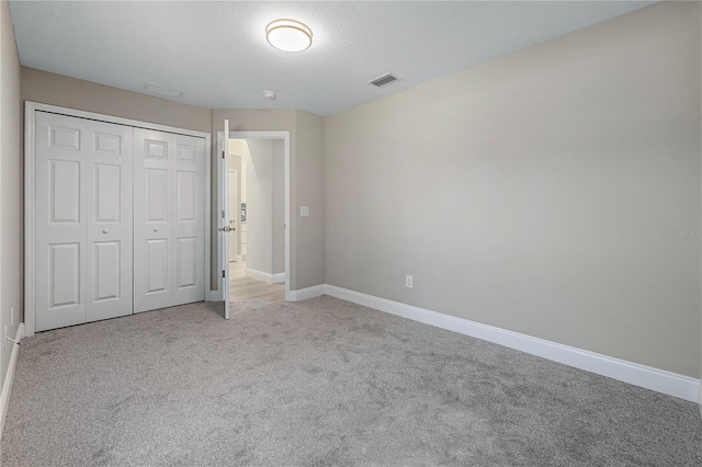 unfurnished bedroom featuring light carpet, baseboards, visible vents, a textured ceiling, and a closet