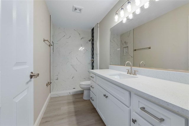 bathroom with toilet, wood finished floors, vanity, visible vents, and a marble finish shower