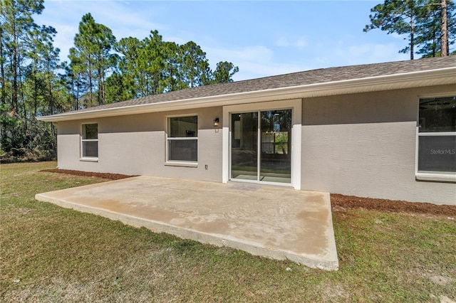 rear view of property featuring a patio, a yard, a shingled roof, and stucco siding