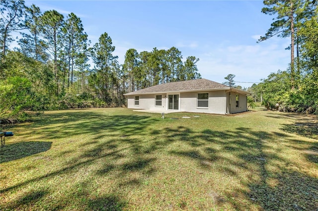 rear view of house with stucco siding and a yard