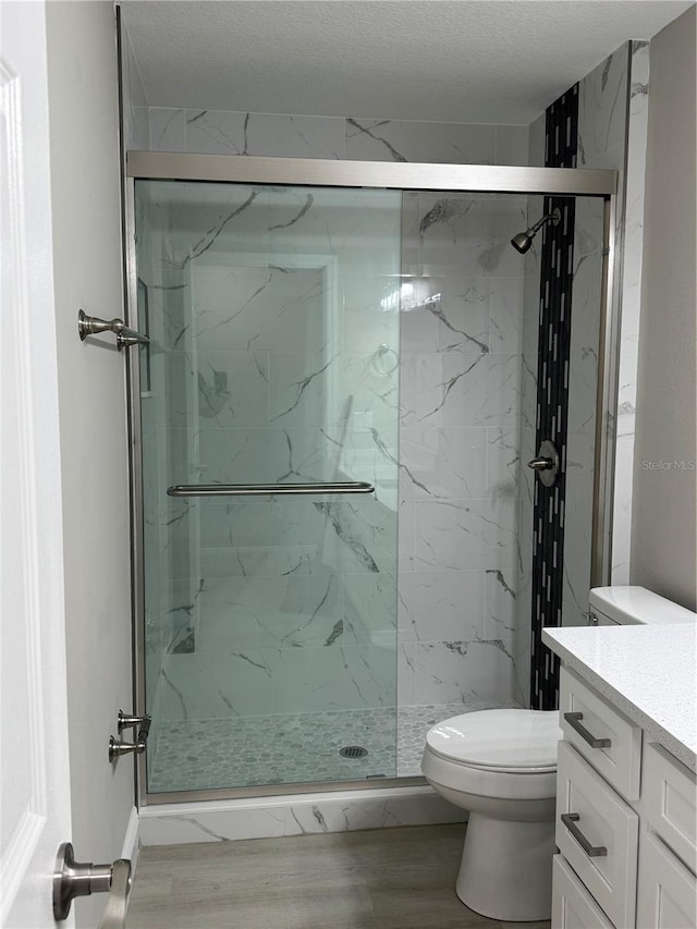 bathroom with toilet, a marble finish shower, wood finished floors, and vanity