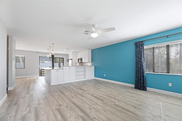 kitchen featuring white cabinets, open floor plan, light countertops, stainless steel microwave, and decorative light fixtures