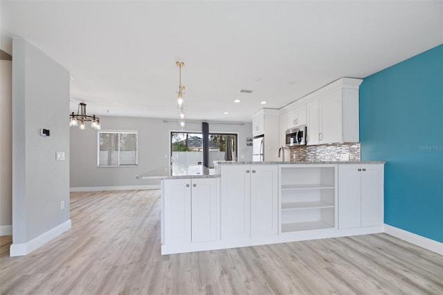 kitchen featuring a peninsula, white cabinetry, tasteful backsplash, stainless steel microwave, and pendant lighting