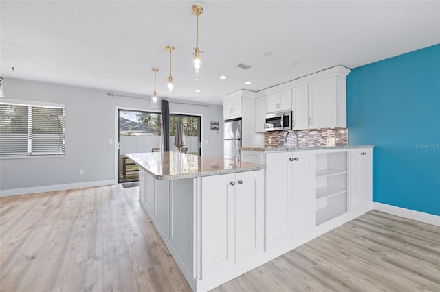 kitchen featuring decorative light fixtures, decorative backsplash, appliances with stainless steel finishes, light wood-style floors, and white cabinetry