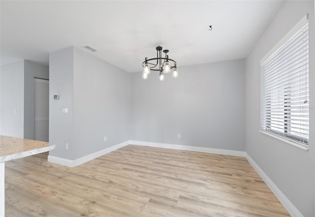 spare room with visible vents, light wood-style flooring, baseboards, and an inviting chandelier