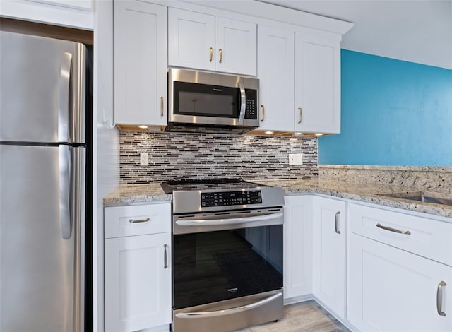 kitchen featuring stainless steel appliances, white cabinets, decorative backsplash, and light stone counters