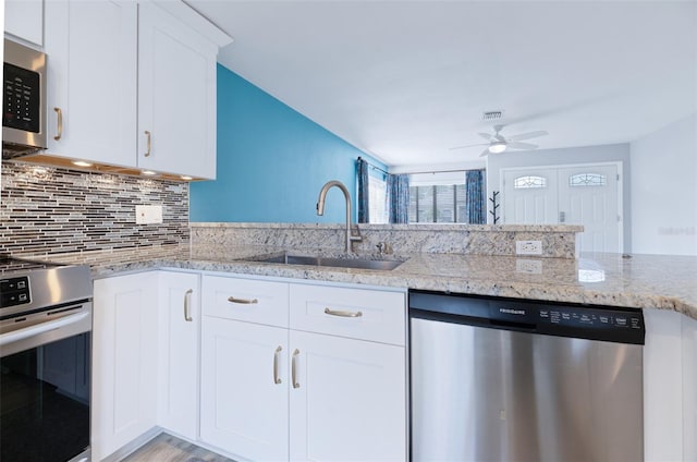 kitchen featuring backsplash, appliances with stainless steel finishes, white cabinetry, a sink, and a peninsula