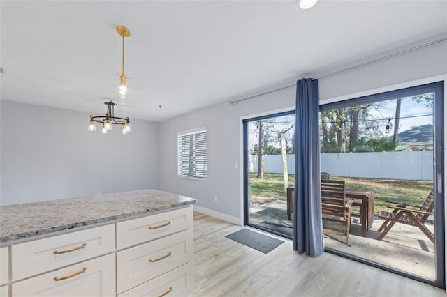 kitchen with white cabinetry, baseboards, light stone countertops, light wood finished floors, and decorative light fixtures