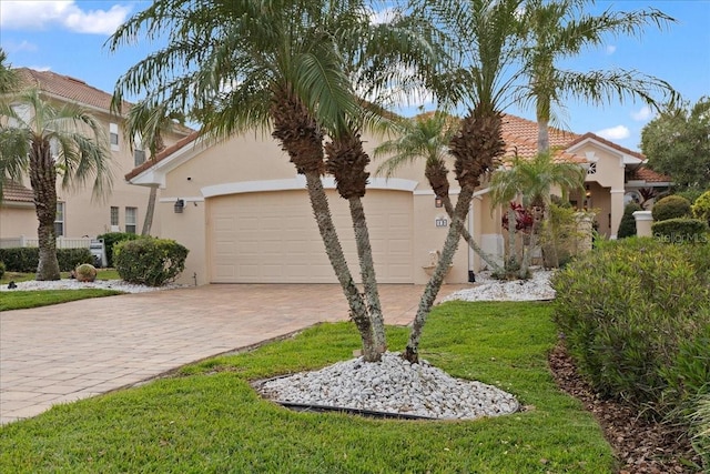 mediterranean / spanish home featuring a front lawn, a tiled roof, stucco siding, decorative driveway, and a garage