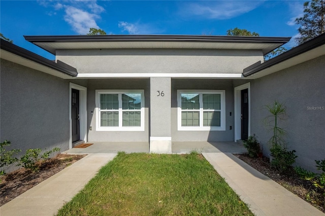 doorway to property with a lawn and stucco siding