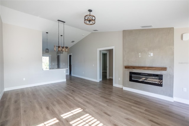 unfurnished living room featuring baseboards, a glass covered fireplace, lofted ceiling, wood finished floors, and a notable chandelier