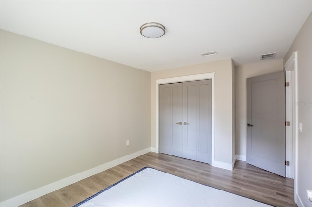 unfurnished bedroom featuring baseboards, a closet, visible vents, and wood finished floors