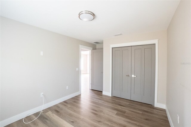 unfurnished bedroom with visible vents, a closet, baseboards, and wood finished floors