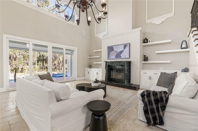 living area featuring a notable chandelier, a towering ceiling, baseboards, and a premium fireplace