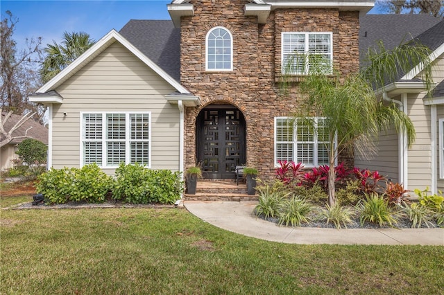 traditional-style home featuring stone siding, a front lawn, and roof with shingles