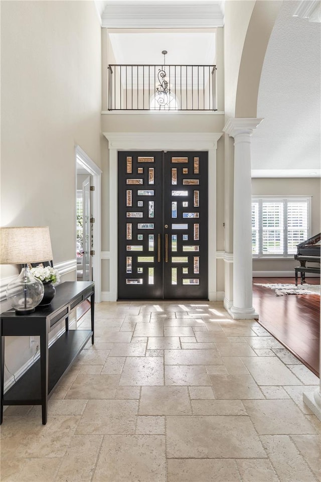 entrance foyer with decorative columns, arched walkways, stone tile flooring, and french doors