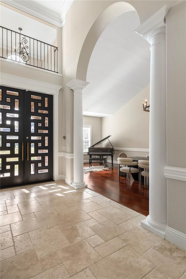 foyer entrance featuring stone tile flooring, baseboards, ornamental molding, french doors, and decorative columns