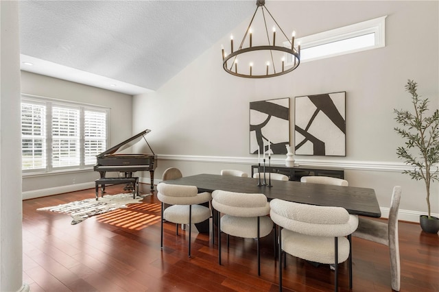 dining space with a notable chandelier, vaulted ceiling, a textured ceiling, wood finished floors, and baseboards