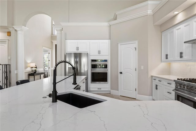 kitchen with stainless steel appliances, a sink, white cabinetry, tasteful backsplash, and ornate columns