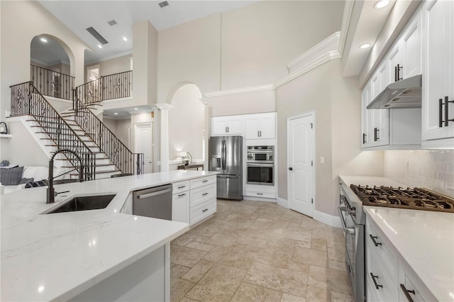 kitchen featuring arched walkways, stainless steel appliances, a sink, under cabinet range hood, and ornate columns