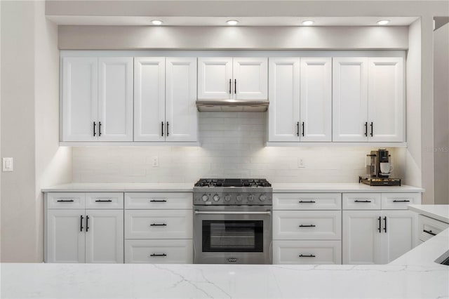 kitchen featuring light stone countertops, under cabinet range hood, white cabinetry, high end stainless steel range oven, and decorative backsplash