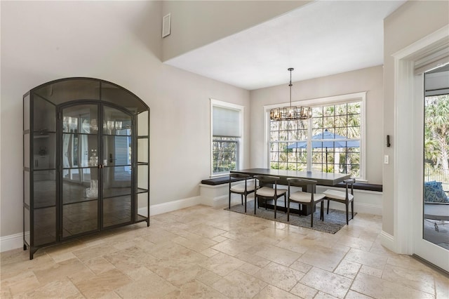 dining space with stone tile flooring, plenty of natural light, baseboards, and an inviting chandelier