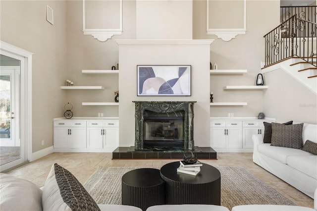 living room featuring a towering ceiling, light tile patterned floors, stairway, and a tile fireplace