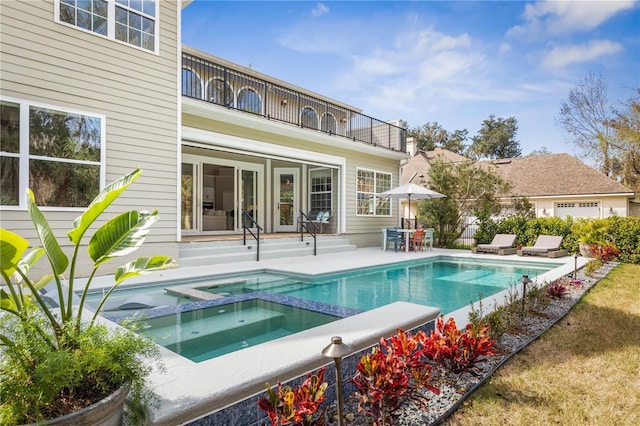 rear view of property featuring a balcony, entry steps, a pool with connected hot tub, and a patio