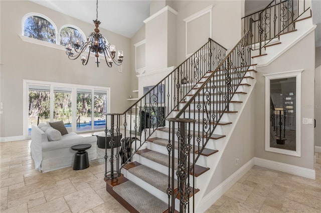 staircase with a towering ceiling, an inviting chandelier, stone tile floors, and baseboards