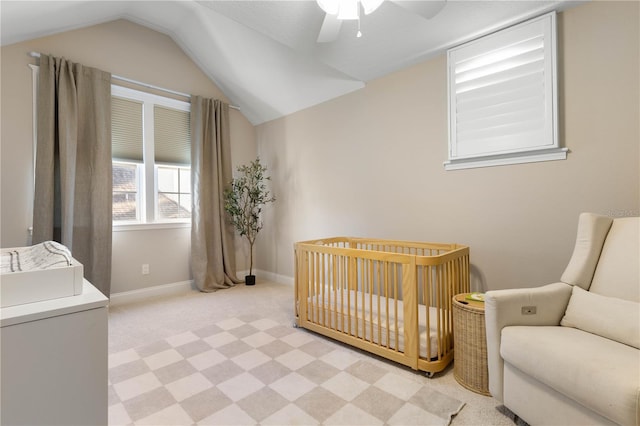 bedroom with light carpet, vaulted ceiling, ceiling fan, a crib, and baseboards