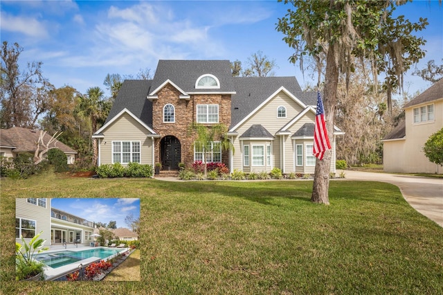 view of front of home with stone siding, roof with shingles, a front yard, and an outdoor pool