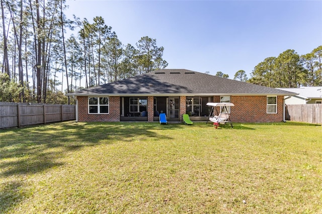 rear view of property with a yard, brick siding, roof with shingles, and a fenced backyard