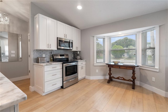 kitchen featuring light wood finished floors, baseboards, appliances with stainless steel finishes, white cabinetry, and backsplash