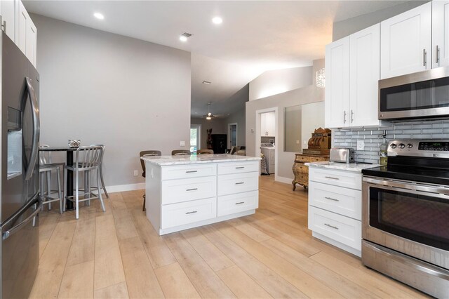 kitchen with light stone counters, lofted ceiling, backsplash, appliances with stainless steel finishes, and light wood-style floors