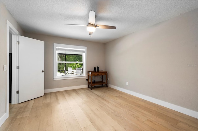 unfurnished room with ceiling fan, a textured ceiling, light wood-style flooring, and baseboards