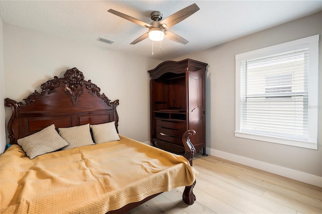 bedroom with baseboards, visible vents, a ceiling fan, a textured ceiling, and light wood-type flooring