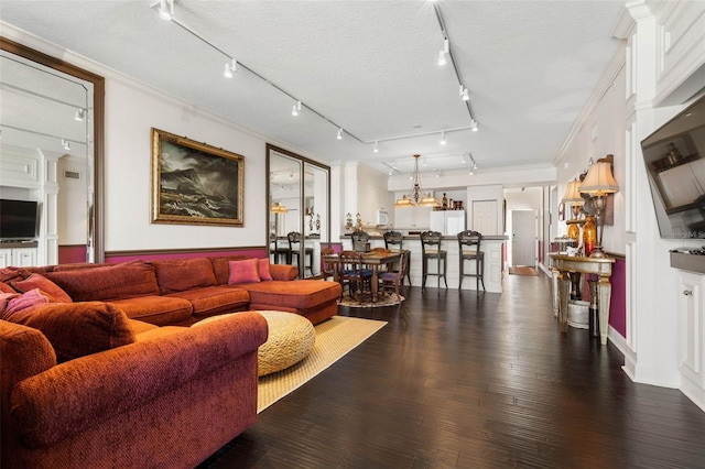 living area featuring dark wood-style flooring, crown molding, a textured ceiling, and ornate columns