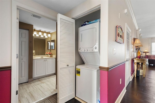 laundry area with laundry area, stacked washer / dryer, a sink, wood finished floors, and crown molding