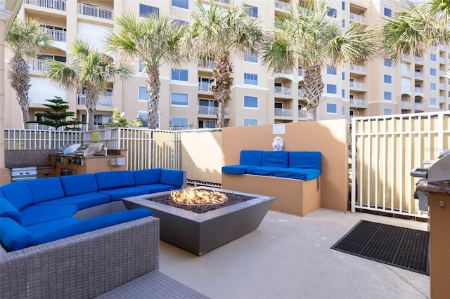 view of patio featuring a grill, an outdoor living space with a fire pit, fence, and an outdoor kitchen