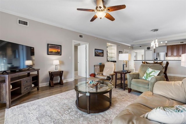 living room featuring light wood-type flooring, visible vents, crown molding, and ceiling fan with notable chandelier