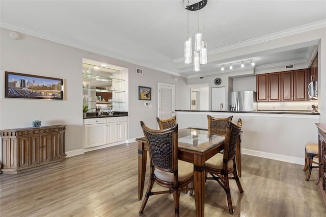 dining area featuring ornamental molding, indoor wet bar, light wood-type flooring, and visible vents