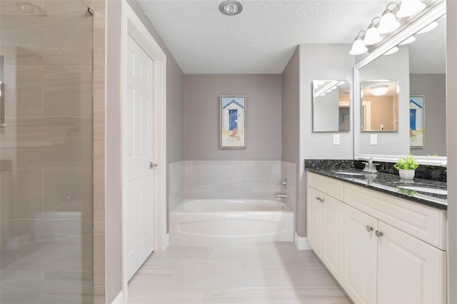 full bathroom featuring a garden tub, vanity, a textured ceiling, and a stall shower