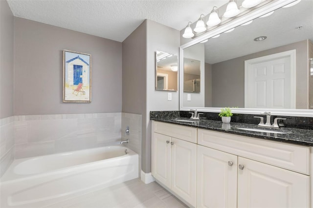 full bath featuring double vanity, a garden tub, a textured ceiling, and a sink