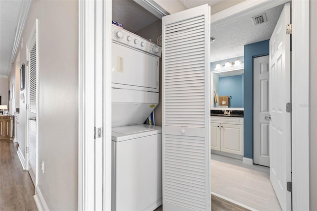 laundry room with a textured ceiling, laundry area, stacked washer / dryer, visible vents, and light wood finished floors