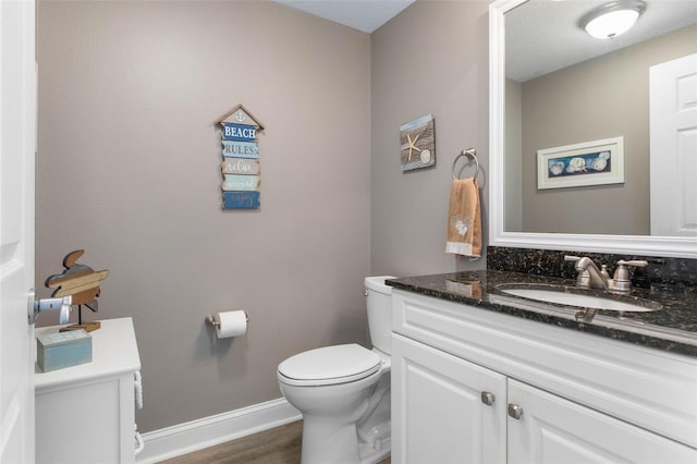 half bath with wood finished floors, vanity, toilet, and baseboards