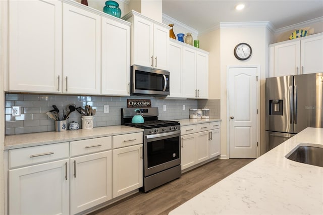 kitchen with stainless steel appliances, white cabinets, ornamental molding, and backsplash