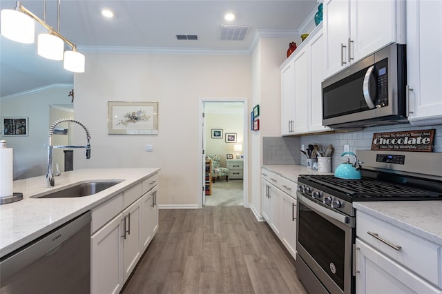 kitchen with a sink, visible vents, appliances with stainless steel finishes, decorative backsplash, and crown molding