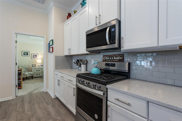 kitchen with light stone counters, stainless steel appliances, tasteful backsplash, ornamental molding, and white cabinets