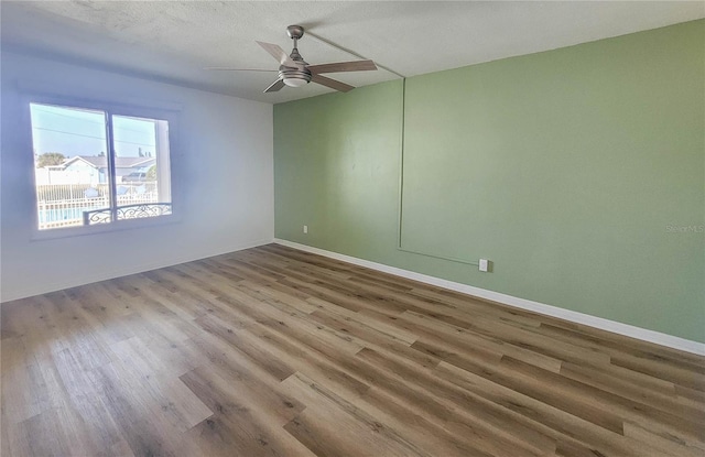 spare room with ceiling fan, a textured ceiling, baseboards, and wood finished floors